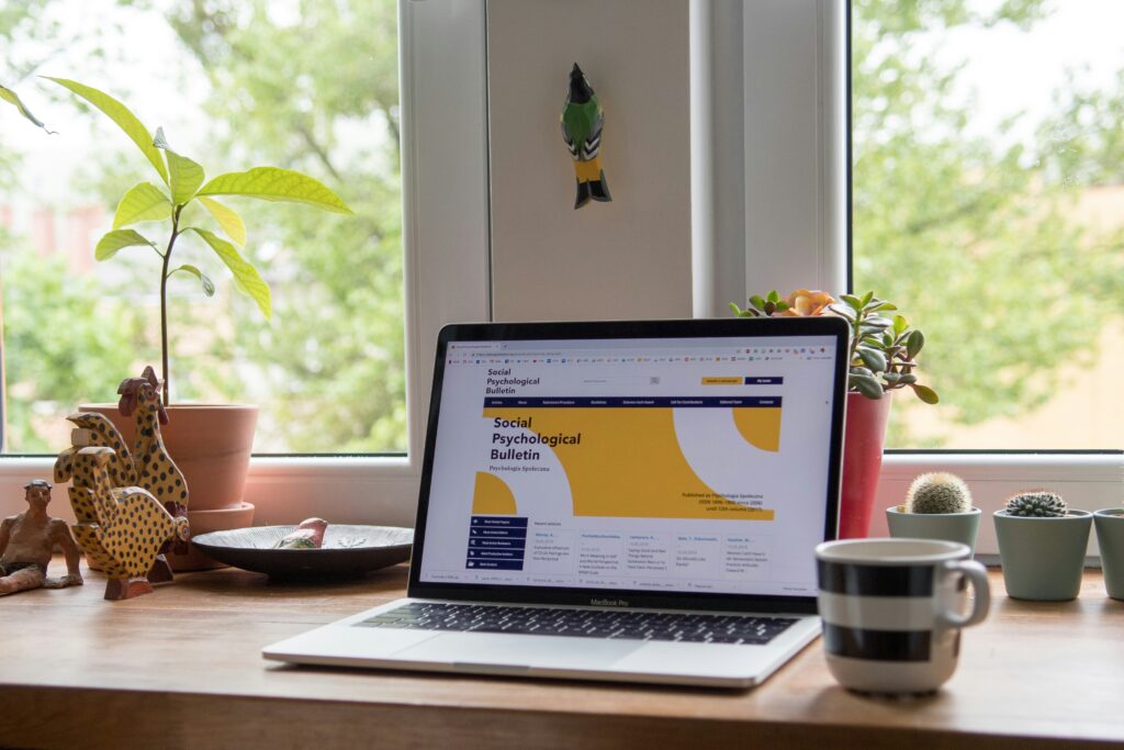 Laptop su scrivania con sito web aperto, tra piante e tazza da caffè