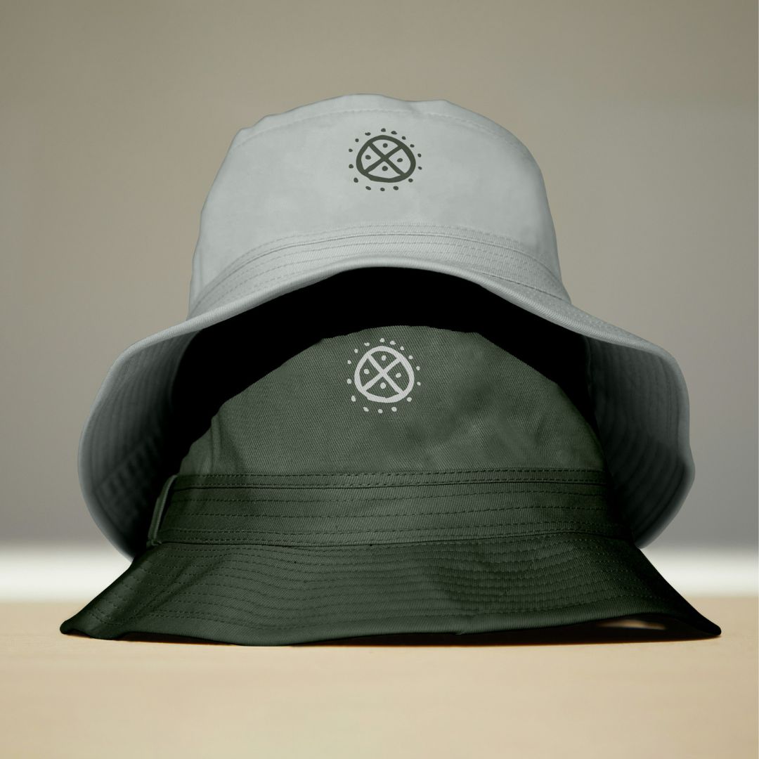 Bucket hat bianchi e verde scuro con il simbolo circolare del brand Solstizio Agency, esempio di declinazione visiva su merchandising.