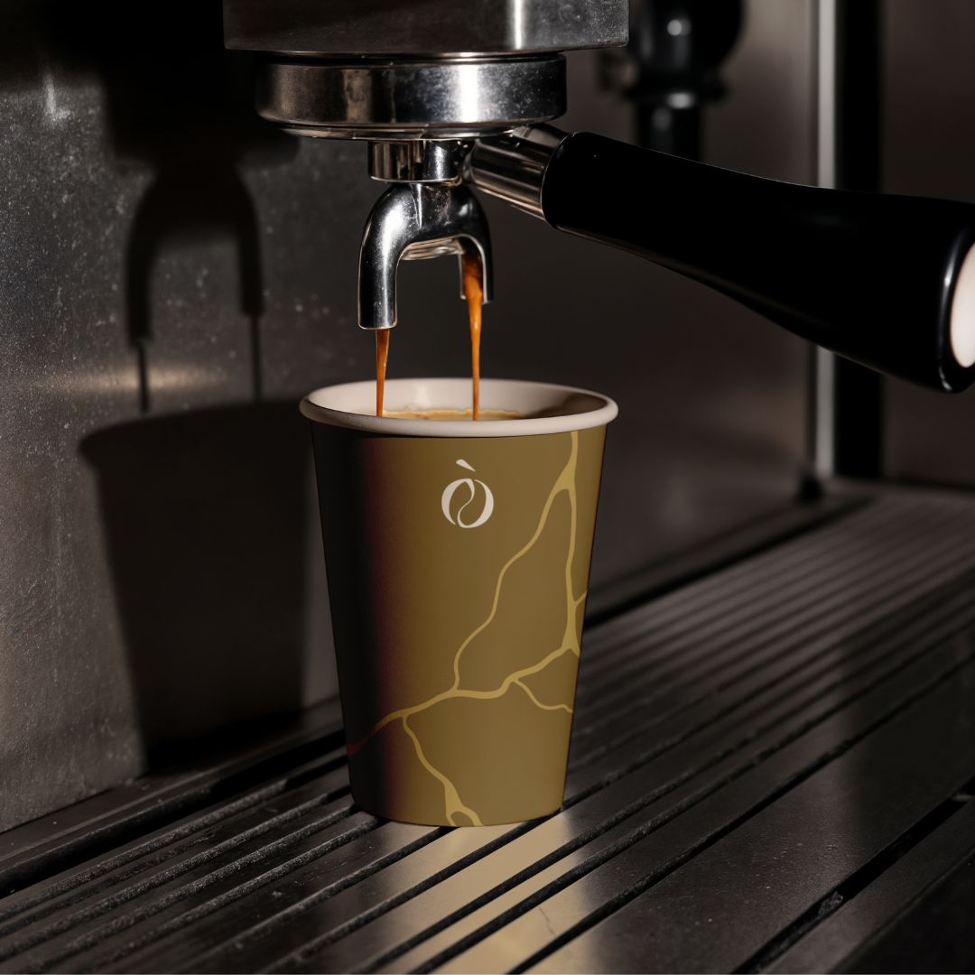 Bicchiere monouso con logo Ribò stampato, posizionato sotto la macchina da espresso. Design caldo e coordinato con il brand.