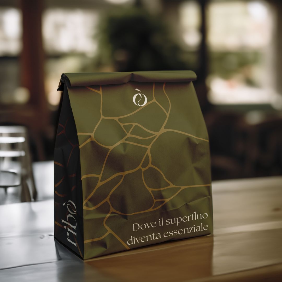 Busta per caffè con logo e payoff del brand Ribò “Dove il superfluo diventa essenziale”, design visivo ispirato al kintsugi.