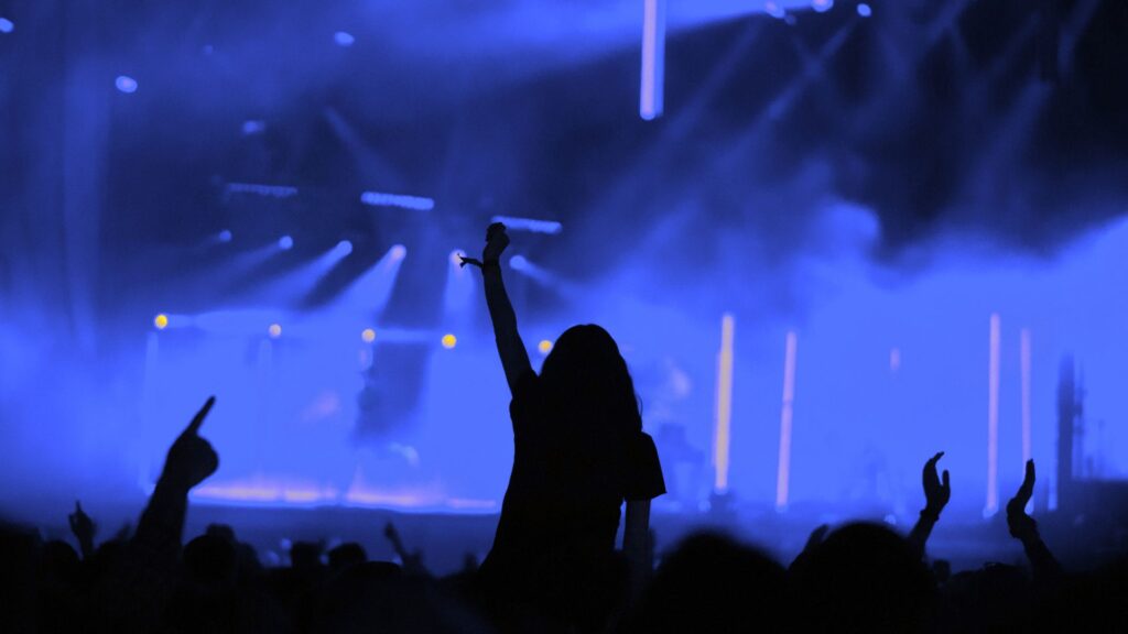 Persona al concerto con mano alzata tra le luci blu, simbolo di visibilità e riconoscibilità del brand