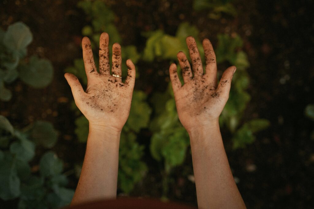 Mani sporche di terra con sfondo naturale, metafora dell’autenticità e del lavoro alla base di un’identità forte