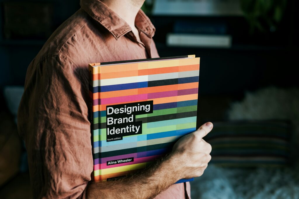 Persona che tiene in mano il libro “Designing Brand Identity” di Alina Wheeler, riferimento nel campo del brand design.
