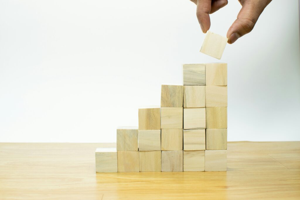 Mano che aggiunge un blocco di legno a una scala di cubi, simbolo della crescita e costruzione del personal branding.